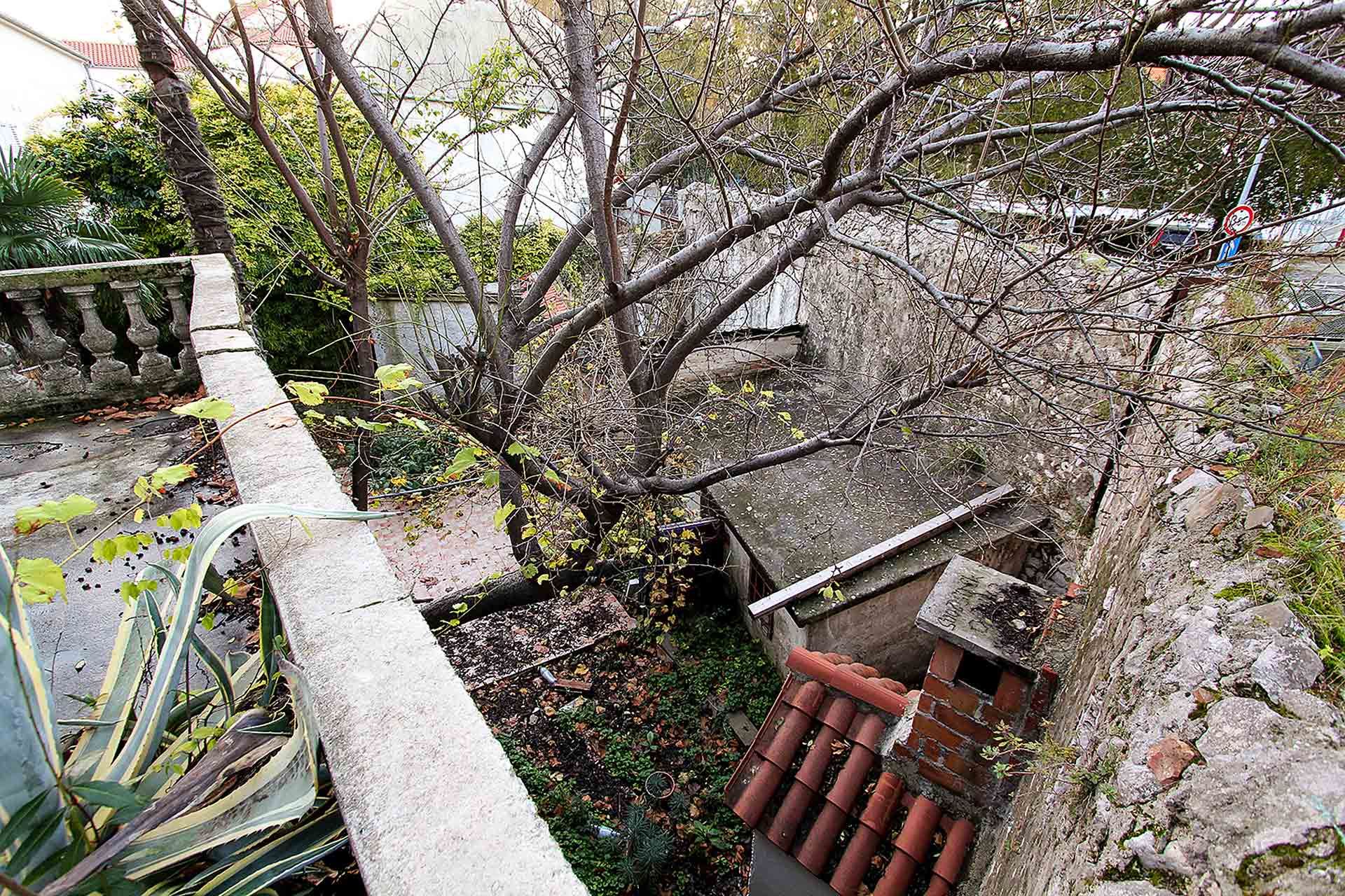 Step into a ruinous courtyard cluttered with layers of various deteriorated buildings, where trees and a fence create a quiet atmosphere. Unbeknownst to many, this hidden gem will soon be transformed into the secret garden of Almayer Art & Heritage H